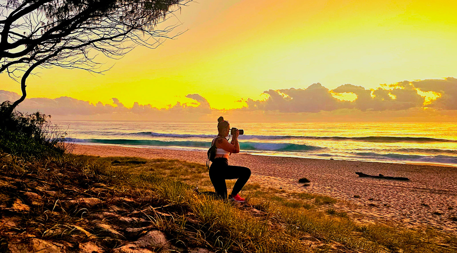 Chantel Elle crouching with her camera, photographing the beach at sunset